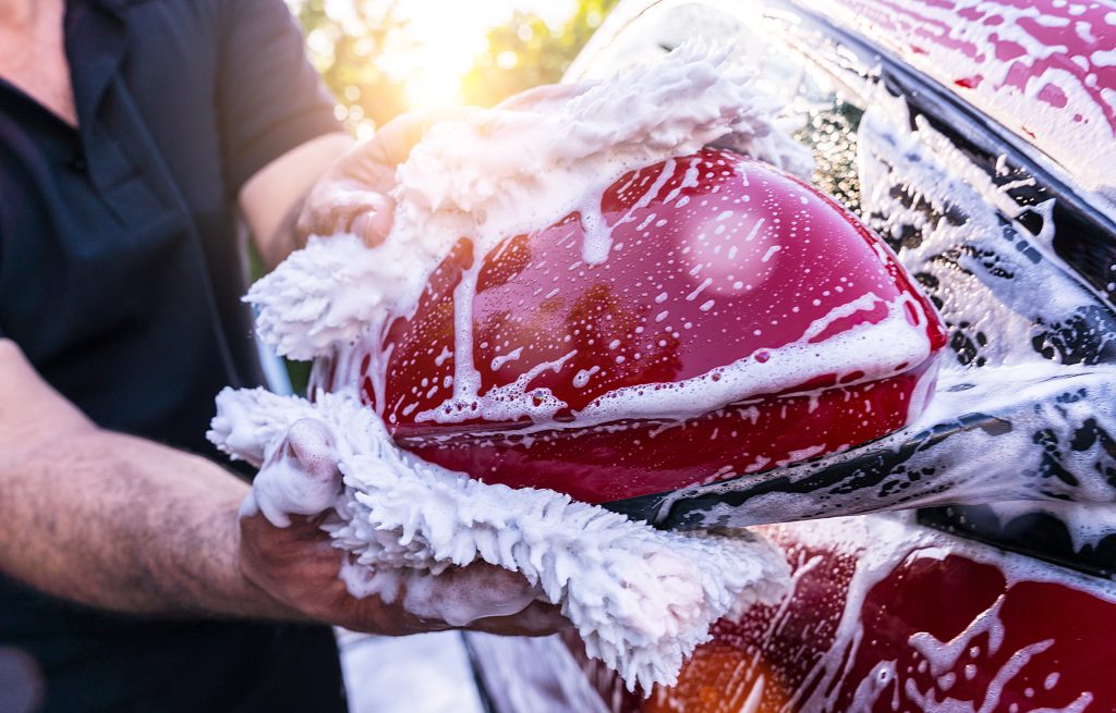 A car being gently washed with a sudsy microfiber mitt, emphasizing careful cleaning and maintenance.
