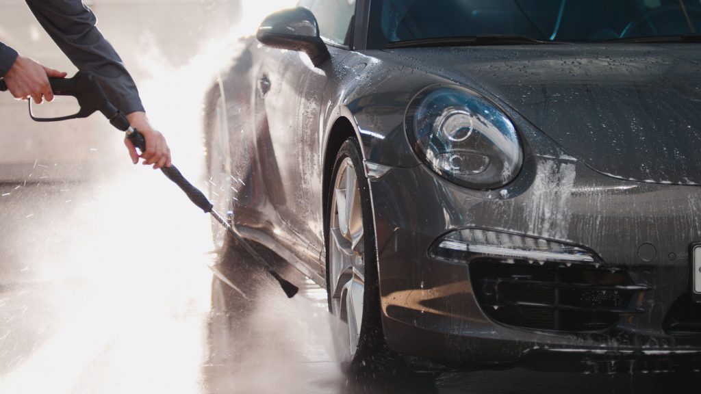 A Porsche being power-washed, focusing on the undercarriage, highlighting Detailing World's comprehensive approach to vehicle maintenance and care.